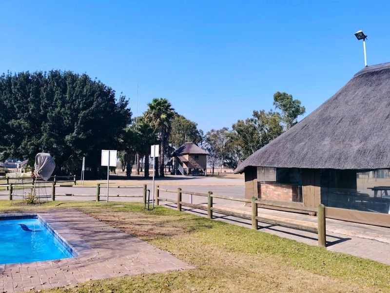 Outdoor pool area featuring a paved surround, timber fencing, and a structure with a traditional thatched roof set in a spacious garden environment.
