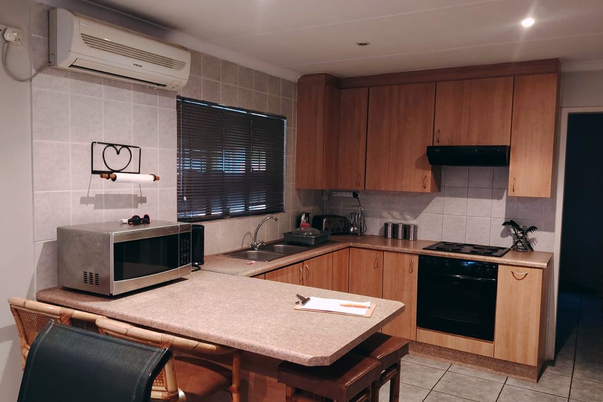 Functional kitchen featuring wood-look cabinetry, laminate countertops, built-in oven with hob, extractor fan, and a convenient breakfast bar area.