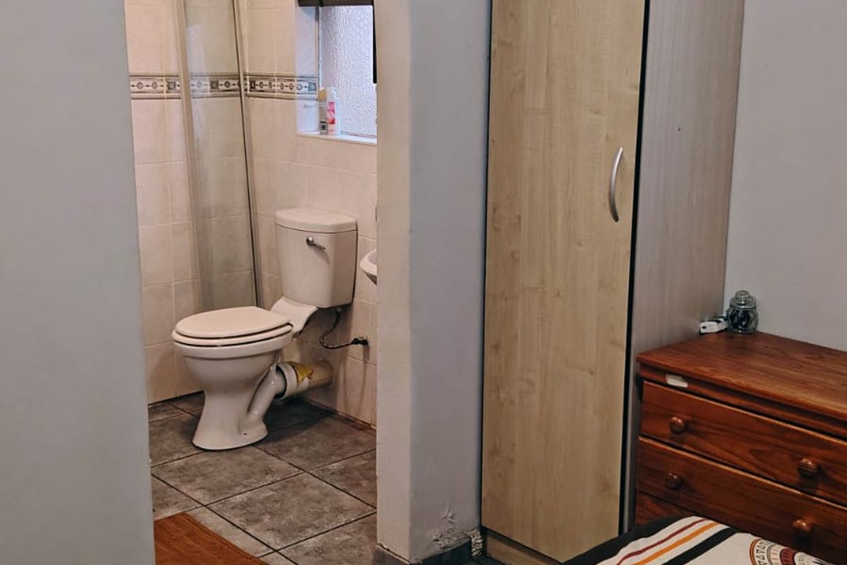 Bedroom featuring an arched entryway leading to an en-suite bathroom with tiled floors, built-in wardrobe, and basic sanitary fixtures.