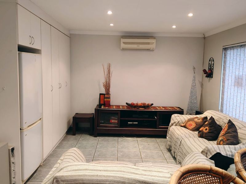 A living room featuring tiled flooring, recessed downlighting, a wall-mounted air conditioning unit, and extensive built-in storage cabinetry.