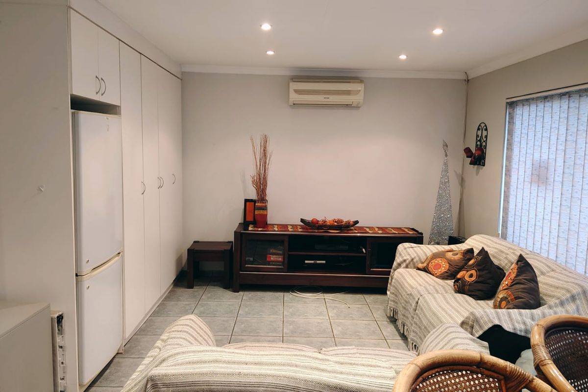 A living room featuring tiled flooring, recessed downlighting, a wall-mounted air conditioning unit, and extensive built-in storage cabinetry.