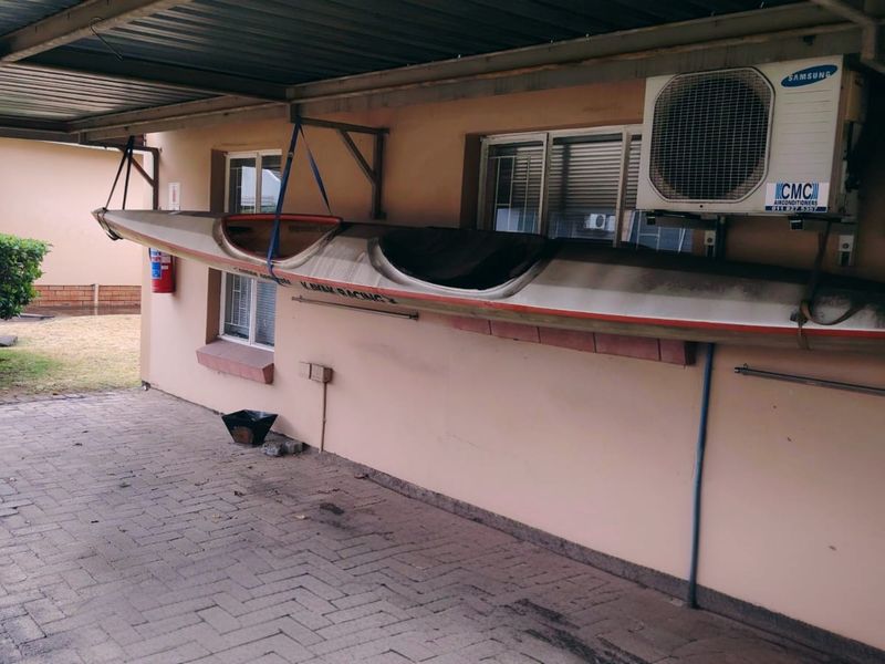 A covered carport area featuring paved flooring, an external air conditioning unit, and a fire extinguisher mounted on the exterior wall.