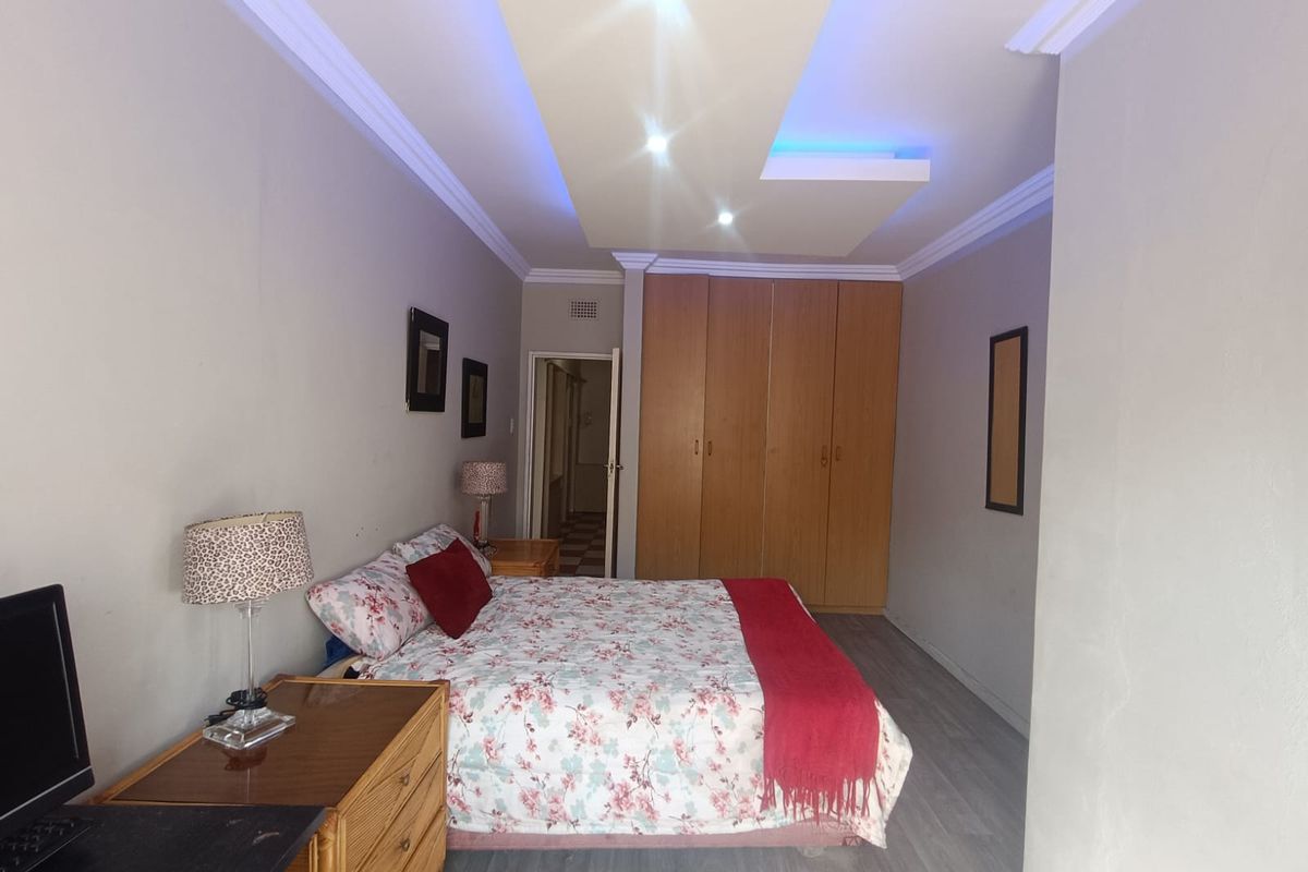 A bedroom featuring built-in wooden cupboards, a recessed ceiling with integrated lighting, and laminate flooring.