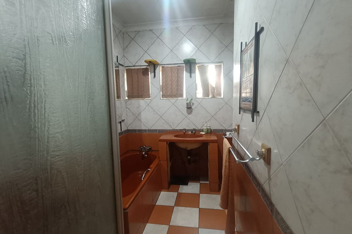 A dated bathroom featuring a built-in bathtub, vanity basin, and tiled finishes throughout, offering potential for a modern renovation.