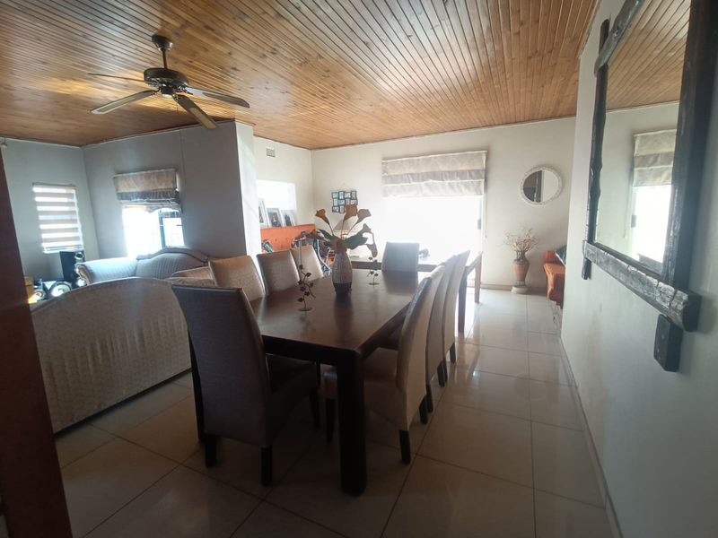 Open plan dining and living area featuring a timber tongue and groove ceiling, tiled flooring, and neutral wall finishes.