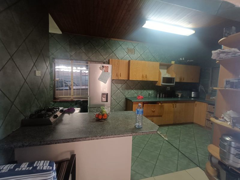 A dated kitchen featuring timber ceilings, tiled walls, and laminate countertops with a gas hob and built-in cabinetry.