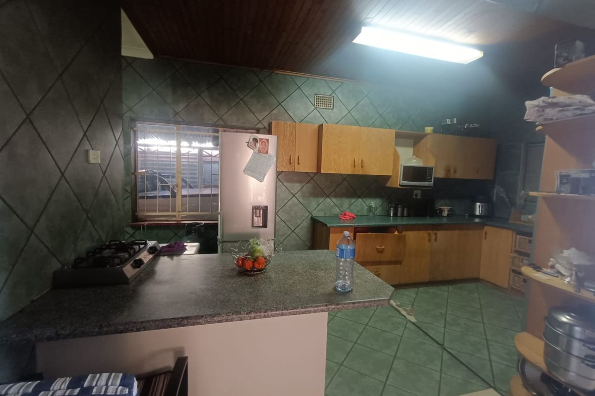 A dated kitchen featuring timber ceilings, tiled walls, and laminate countertops with a gas hob and built-in cabinetry.