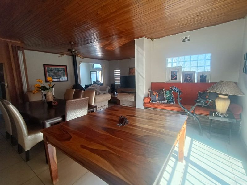Spacious open-plan living and dining area featuring a distinctive timber tongue and groove ceiling, tiled flooring, and a unique glass block window feature.