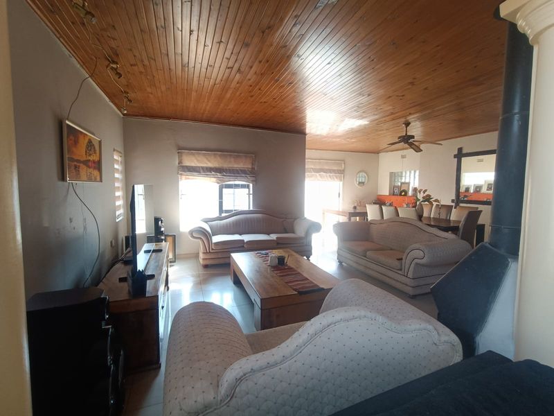 Spacious open-plan living and dining area featuring a warm timber-clad ceiling, tiled flooring, and a prominent freestanding fireplace.