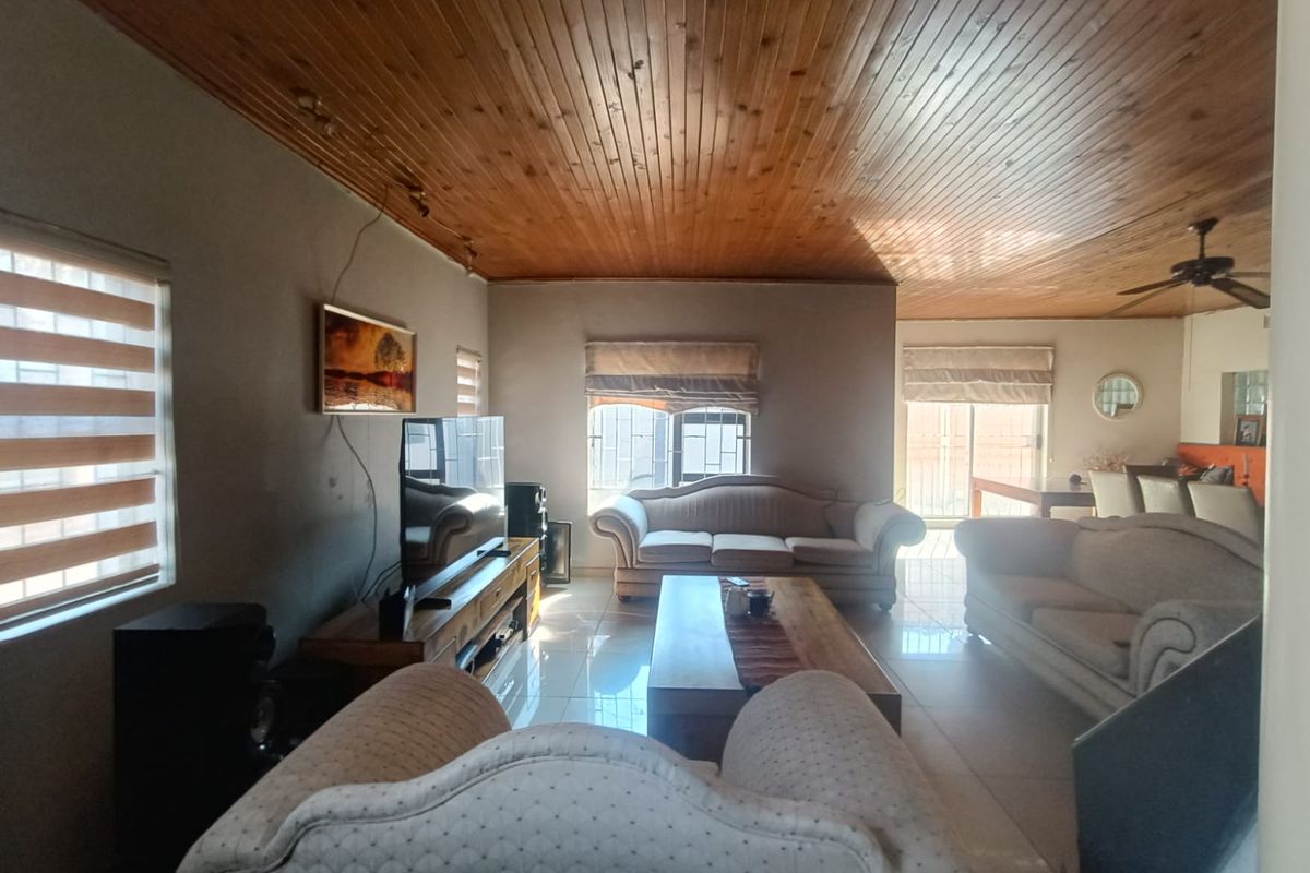 Spacious living room featuring a timber tongue and groove ceiling, tiled flooring, and a ceiling fan, with natural light from multiple windows.