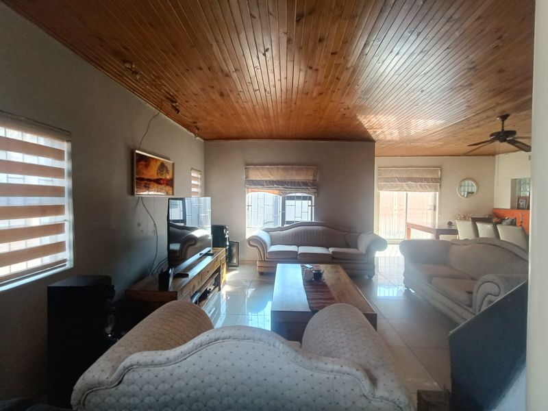 Spacious living room featuring a timber tongue and groove ceiling, tiled flooring, and a ceiling fan, with natural light from multiple windows.