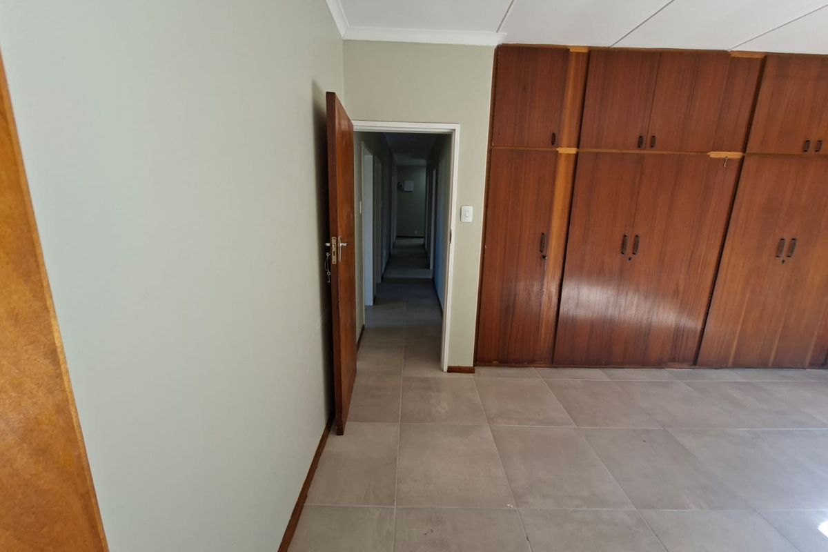 A spacious bedroom featuring large built-in wooden cupboards, neutral tiled flooring, and direct access to the hallway.