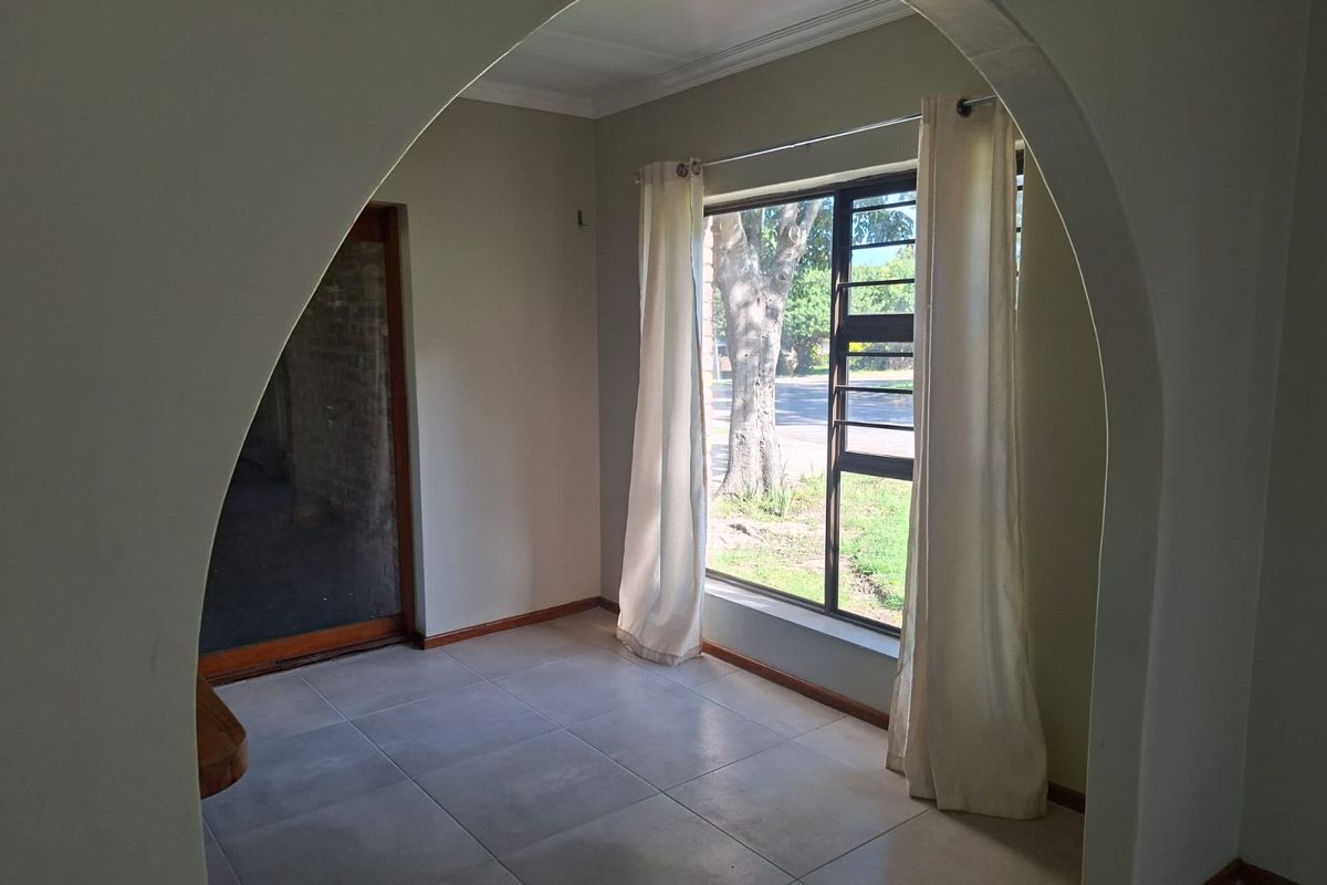 A bright, empty living area featuring a distinctive arched doorway, neutral tiled flooring, and large windows providing natural light.