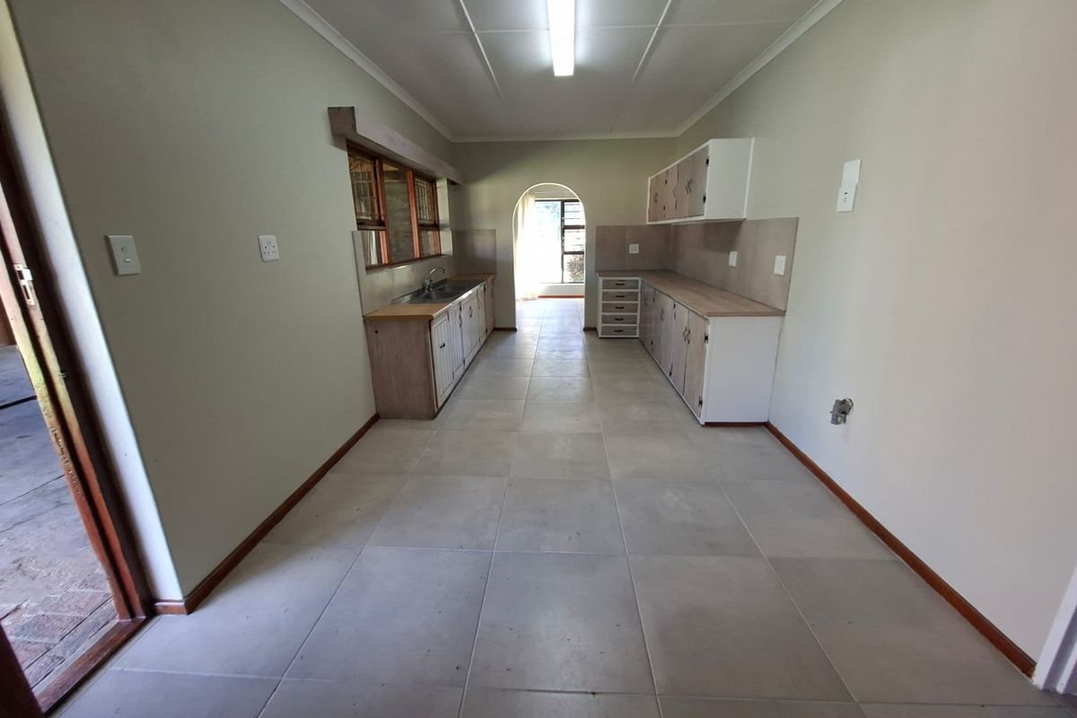 A functional, empty kitchen featuring tiled flooring, laminate countertops, built-in cabinetry, and a stainless steel sink, offering a blank canvas for modern updates.