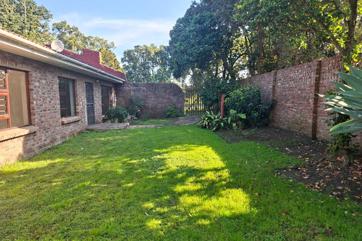 A private rear garden featuring a well-maintained lawn, enclosed by high brick boundary walls and mature trees, offering a secluded outdoor space.