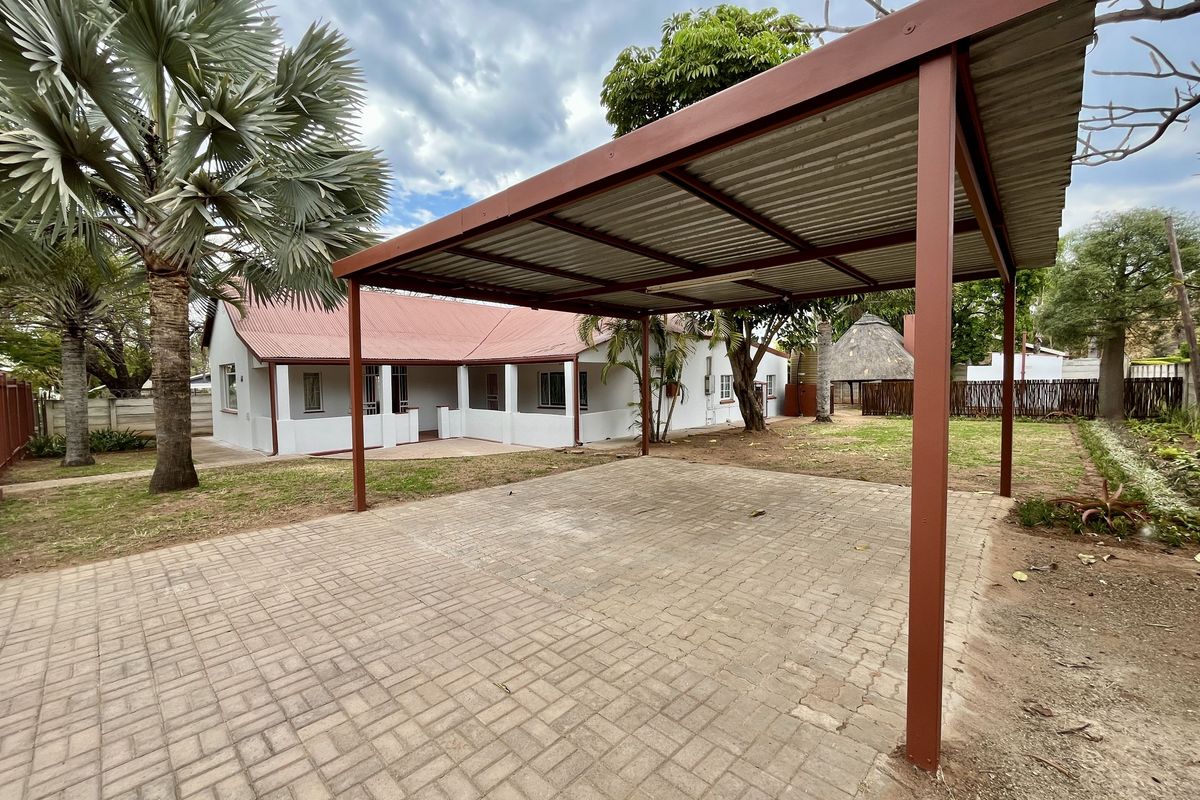 A rear exterior view featuring a metal carport structure over a paved driveway, adjacent to the main house with a covered patio area.