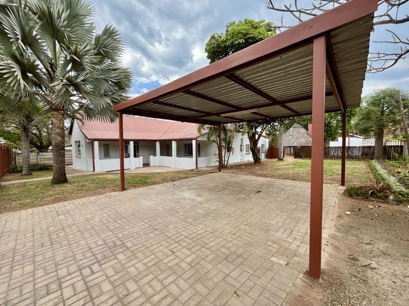 A rear exterior view featuring a metal carport structure over a paved driveway, adjacent to the main house with a covered patio area.
