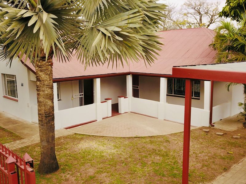 Front view of a residential house featuring a covered patio, corrugated metal roof, paved driveway, and a carport.