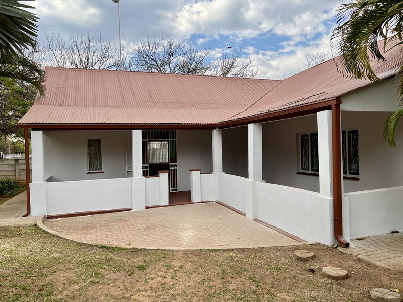 A rear view of the house featuring a covered patio with brick paving, corrugated metal roofing, and security features on windows and doors.