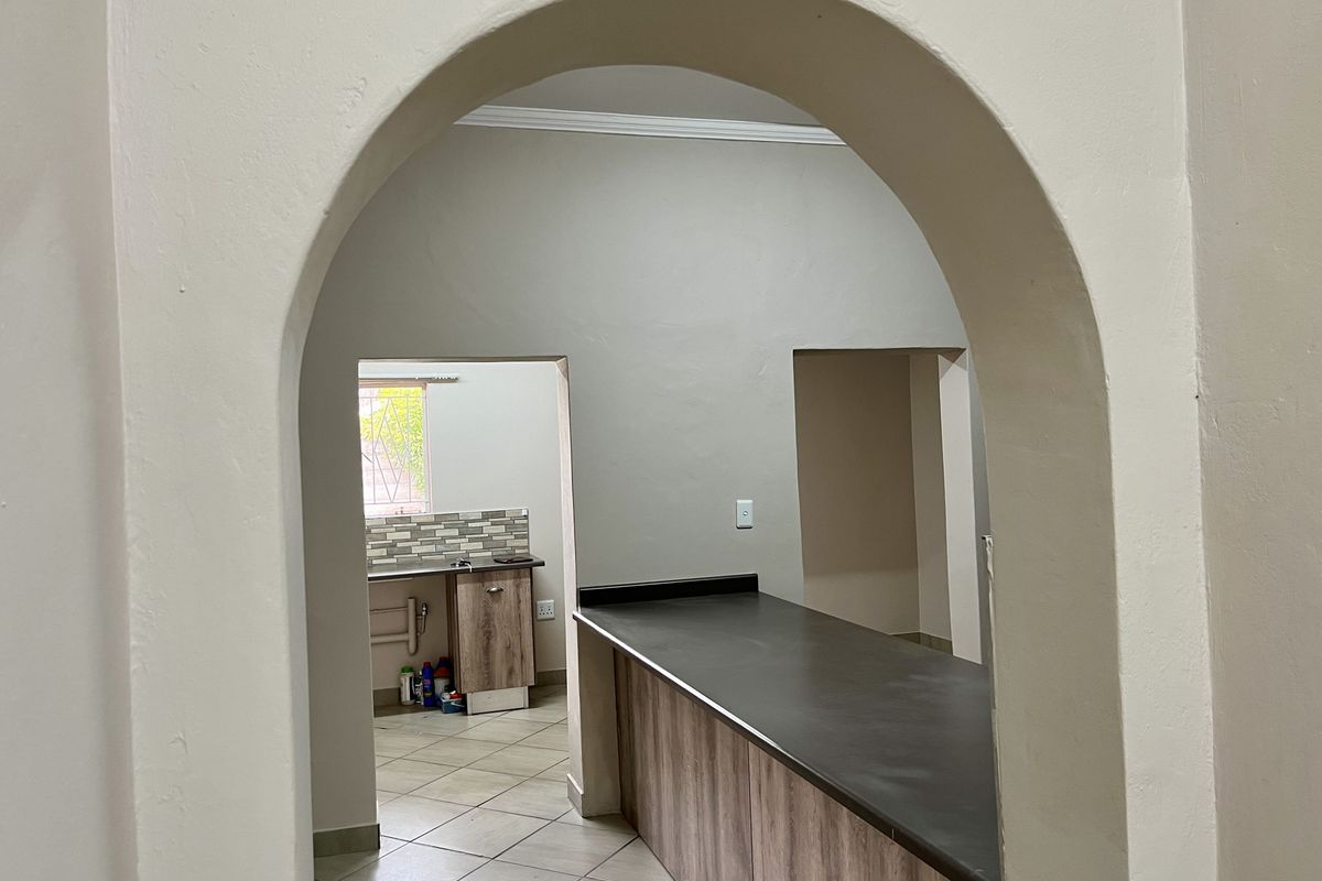 A view through an arched doorway into a kitchen featuring wood-look cabinetry, dark countertops, and tiled flooring.