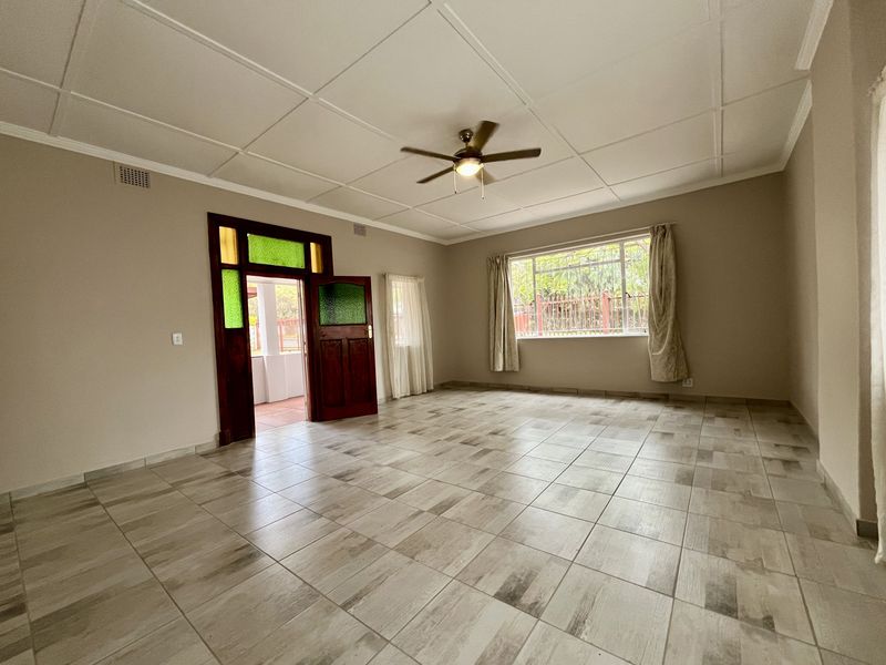 Spacious living room featuring neutral tiled flooring, a ceiling fan, and a classic timber door with decorative stained glass inserts.