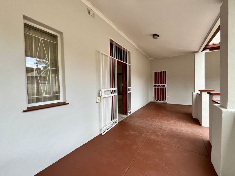 A covered patio area featuring tiled flooring, security gates, and security bars on the windows, providing a secure outdoor transition space.