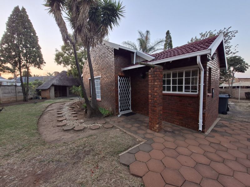 A rear view of a face brick house featuring a paved patio area, security gate, and a landscaped garden path.