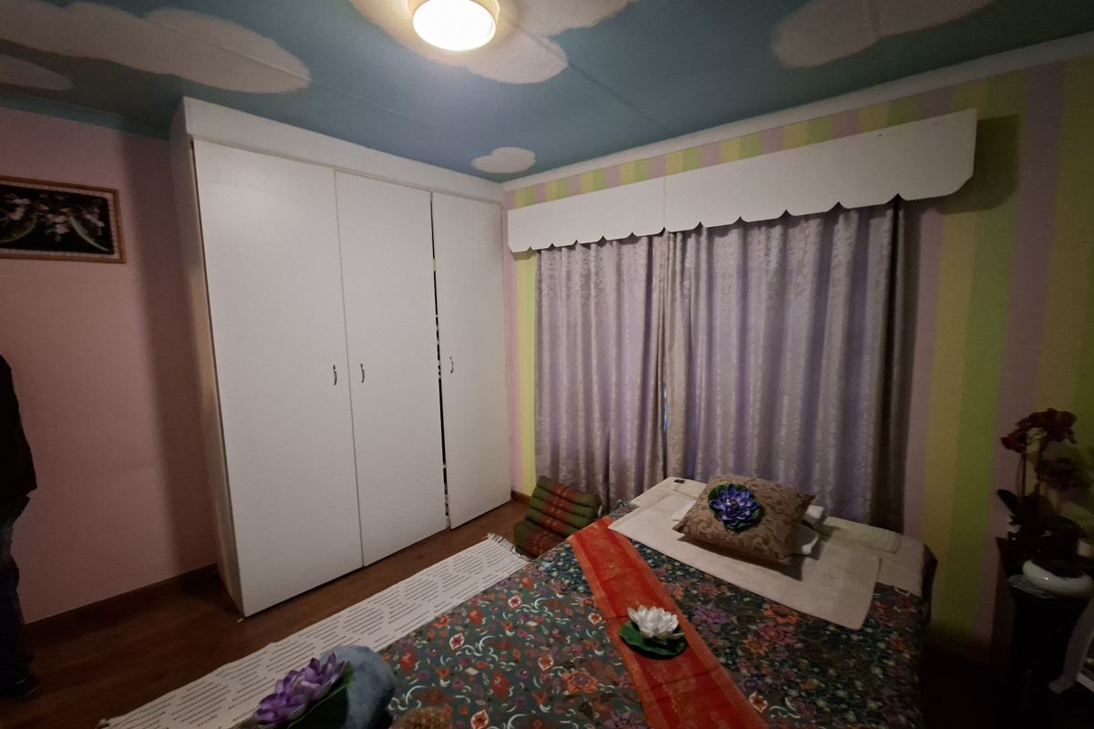 A bedroom featuring hardwood flooring and a large white built-in wardrobe, with a decorative painted ceiling and window pelmet.