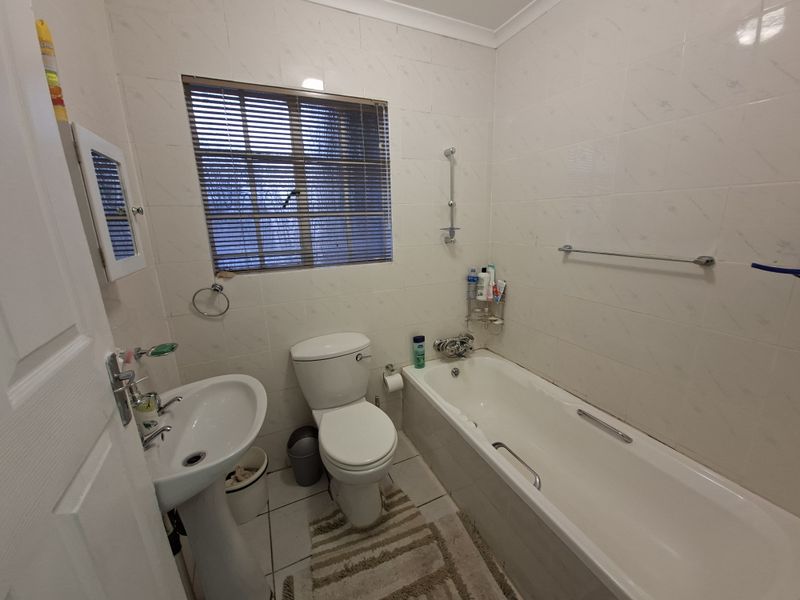 A functional bathroom featuring a pedestal basin, toilet, and bathtub with full-height wall tiling and a window for natural light.