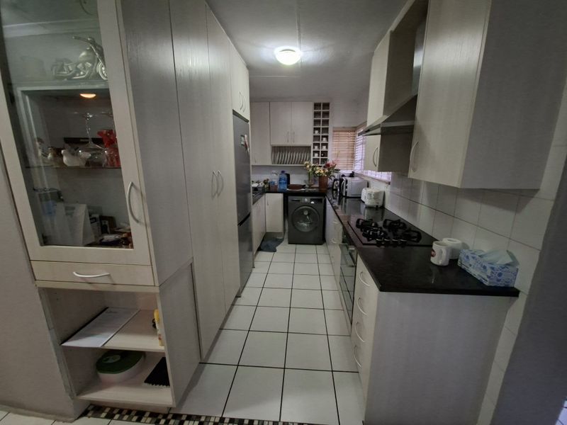 A functional galley-style kitchen featuring built-in cabinetry, granite countertops, a gas hob, and integrated oven, with tiled flooring throughout.