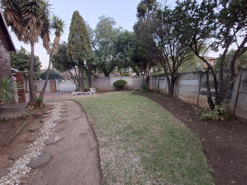 A private rear garden featuring a lawn area, mature trees, and a precast concrete boundary wall with a paved side access path.