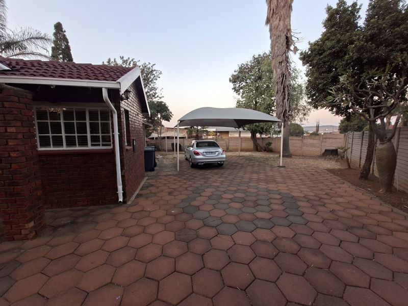 Rear exterior area featuring brick paving, a shade port for vehicle parking, and a brick boundary wall.