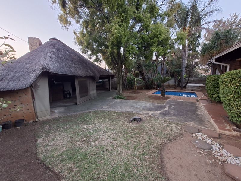 Rear garden area featuring a thatched lapa, paved patio space, and a swimming pool set within a landscaped yard.