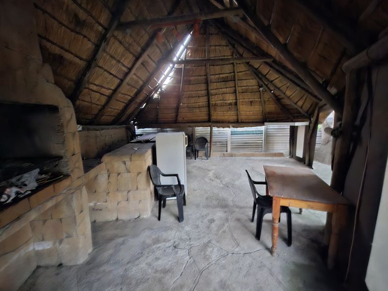 Covered outdoor entertainment area featuring a traditional thatched roof, exposed timber rafters, and a built-in stone braai station.