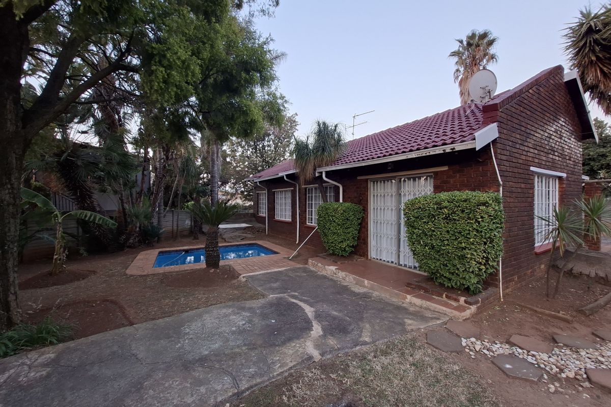 Rear view of a brick house featuring a swimming pool, tiled roof, and sliding glass doors leading to the garden area.