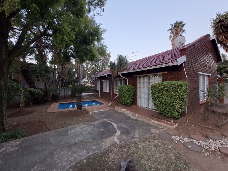 Rear view of a brick house featuring a swimming pool, tiled roof, and sliding glass doors leading to the garden area.