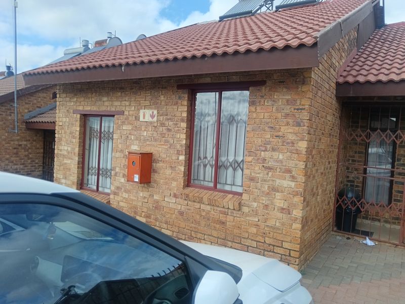 Front elevation of a face brick townhouse featuring a tiled roof, solar water heating system, and secure window gates.