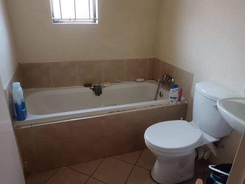 A functional bathroom featuring a built-in bathtub, toilet, and basin with neutral ceramic tiling throughout.