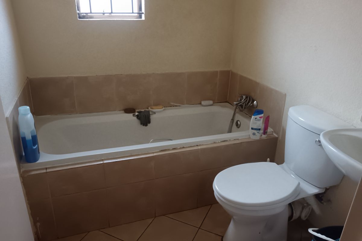 A functional bathroom featuring a built-in bathtub, toilet, and basin with neutral ceramic tiling throughout.