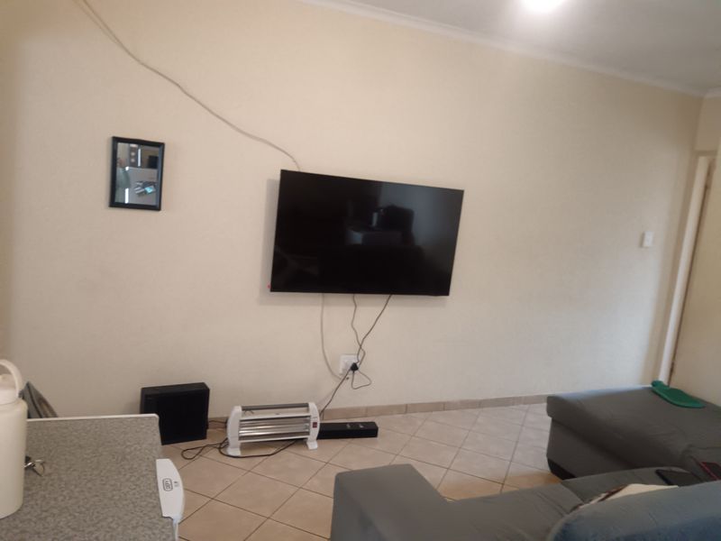 A living room area featuring tiled flooring and wall-mounted television setup with visible electrical cabling.
