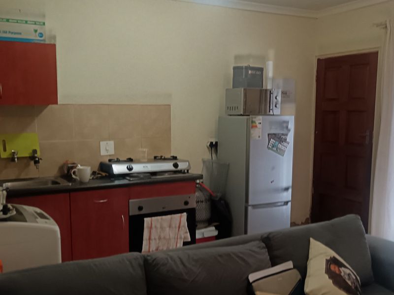Open-plan living area featuring a compact kitchen with red cabinetry, gas hob, and built-in oven, adjacent to a living space with direct door access.