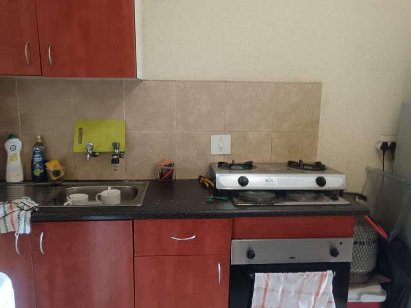 A functional kitchen featuring laminate cabinetry, a stainless steel sink, tiled backsplash, and a built-in gas hob with oven.