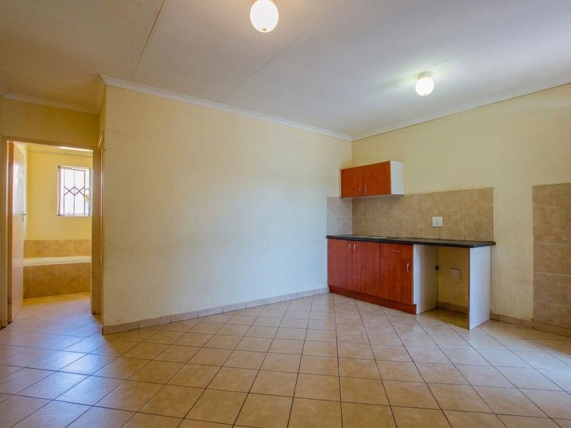 An open-plan living area featuring a compact kitchenette with built-in cabinetry, tiled flooring, and direct access to an adjacent bathroom.