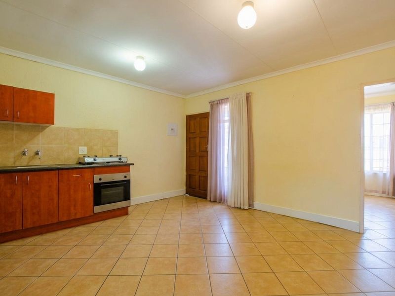 Open-plan kitchen and living area featuring tiled flooring, built-in cabinetry with integrated oven and hob, and direct access to an adjoining room.