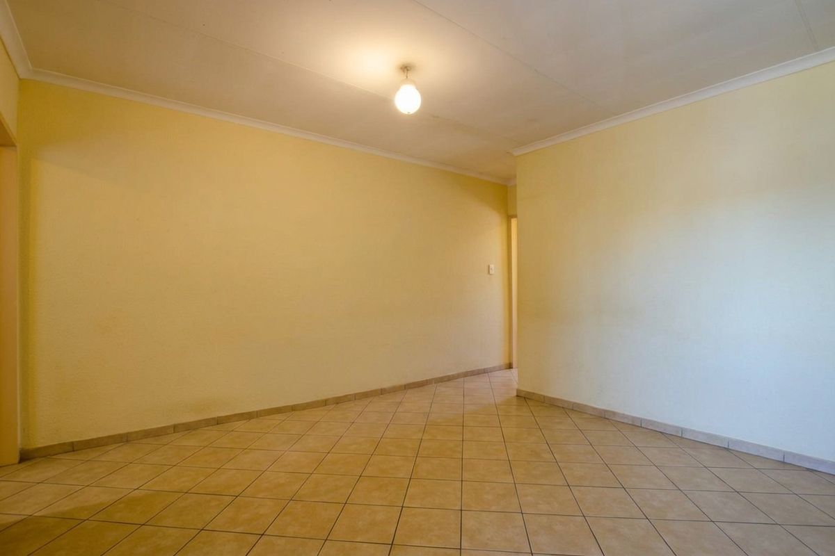 An empty, neutrally painted living area featuring ceramic floor tiles and coved ceiling cornices, offering a blank canvas for interior design.