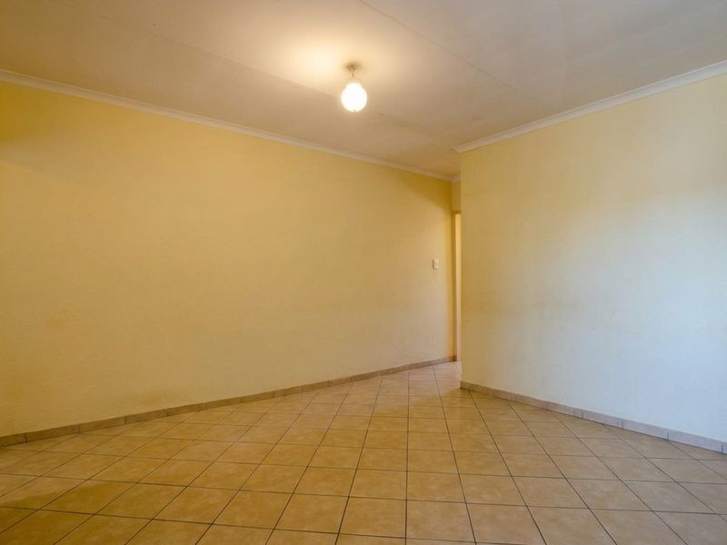 An empty, neutrally painted living area featuring ceramic floor tiles and coved ceiling cornices, offering a blank canvas for interior design.