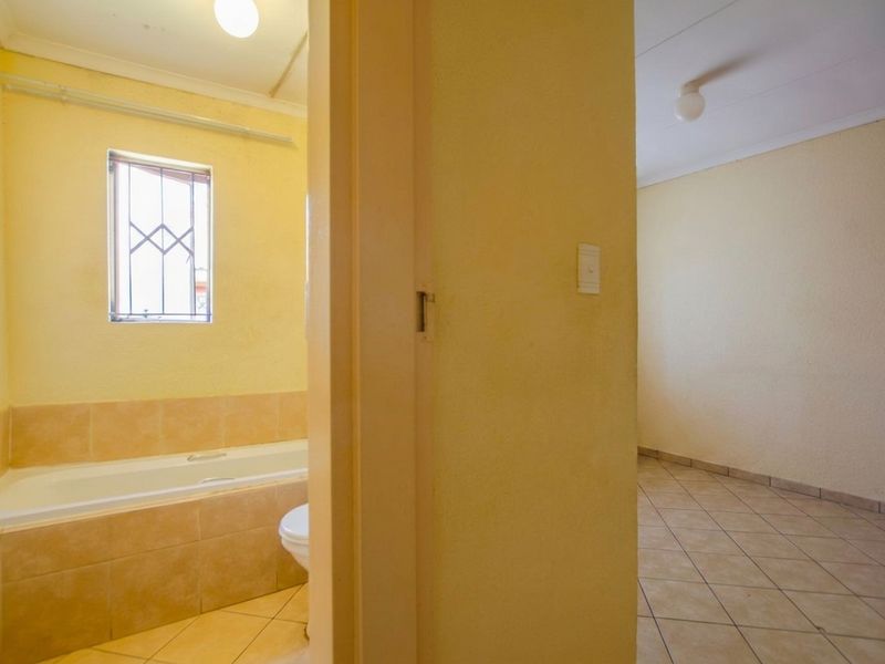 A vacant bathroom featuring a built-in bathtub with tiled surround and ceramic floor tiles, adjacent to an empty tiled room.