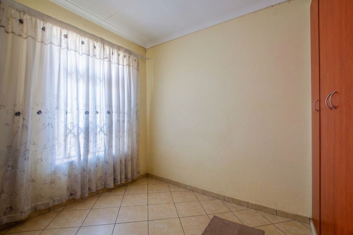 A clean, empty bedroom featuring neutral tiled flooring, a built-in wardrobe, and a large window with curtains.