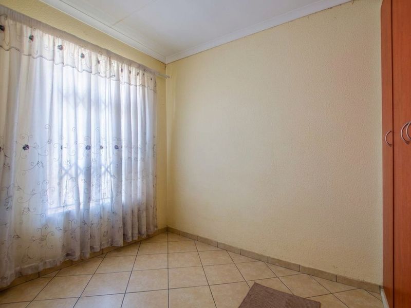 A clean, empty bedroom featuring neutral tiled flooring, a built-in wardrobe, and a large window with curtains.