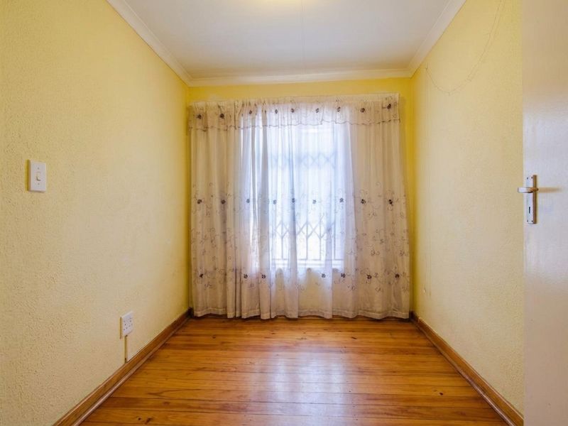 An empty bedroom featuring original timber flooring, yellow painted walls, and a window fitted with a security gate.